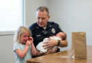 A Little Girl Walked Into a Police Station Holding a Paper Bag and Whispered, “Please Help… My Baby Brother Stopped Moving” — What Officers Discovered About Her Family Left Everyone Silent